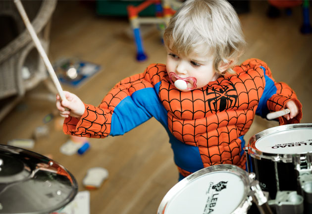 Pojke i spindelmannen-dräkt som spelar trummor