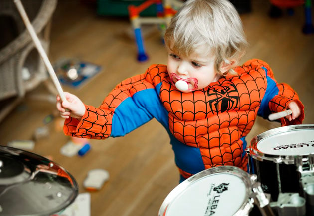 Pojke i spindelmannen-dräkt som spelar trummor