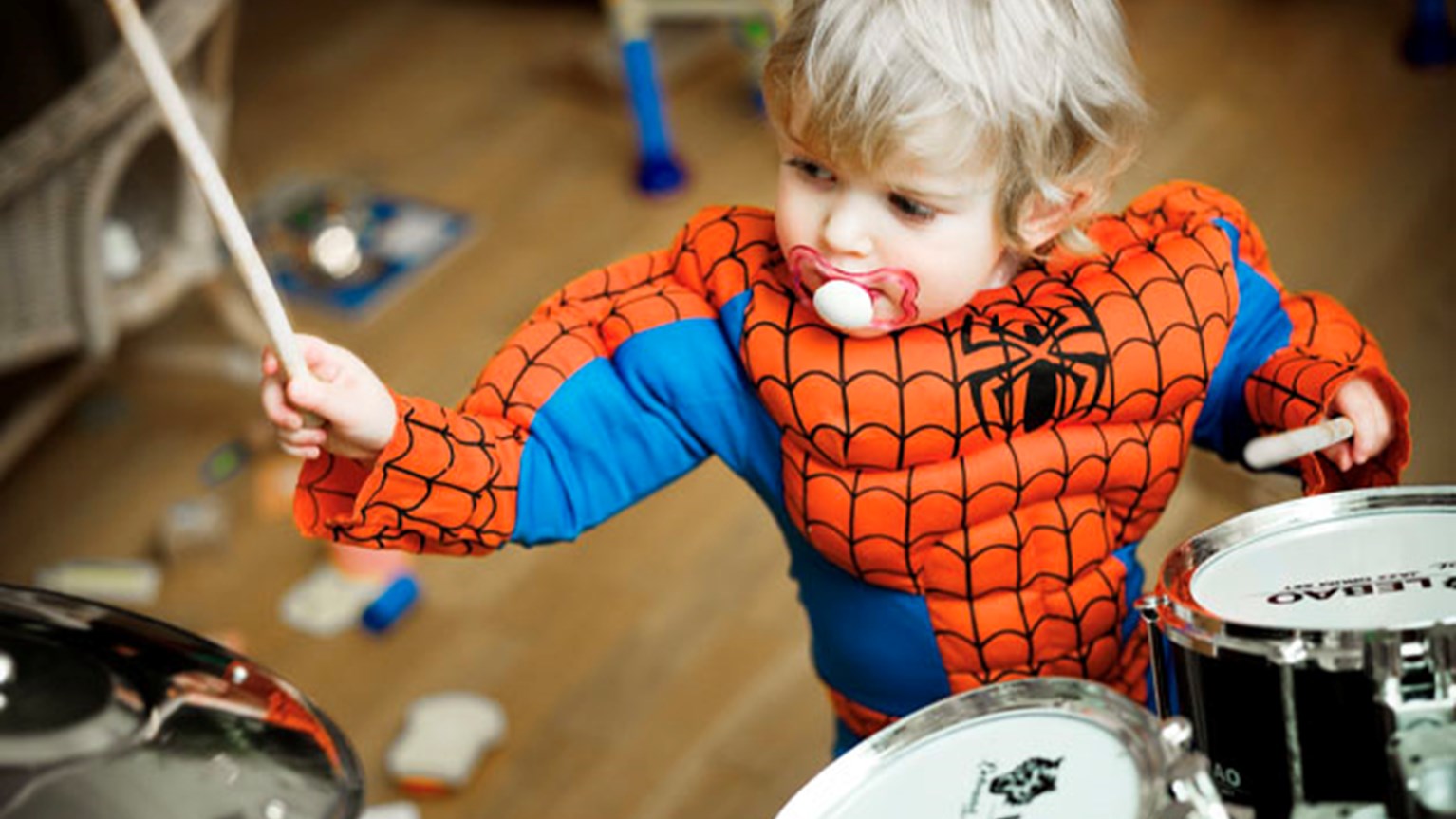 Pojke i spindelmannen-dräkt som spelar trummor